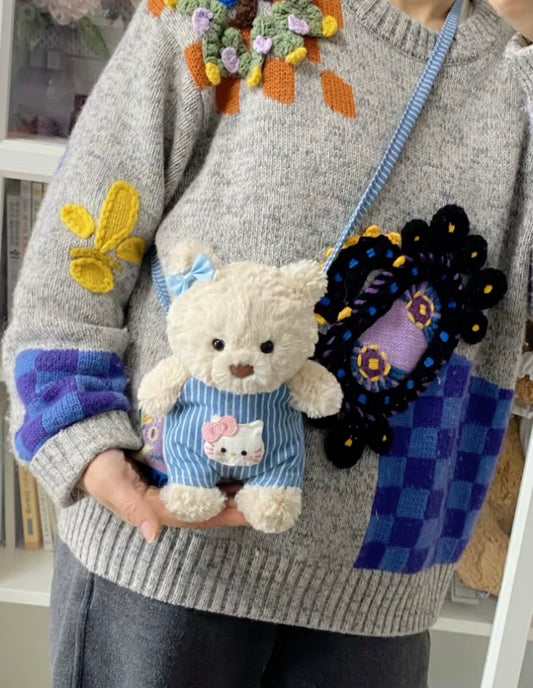Jellycat bear wearing blue striped dungaree with Hello Kitty patch, held by person wearing grey sweater