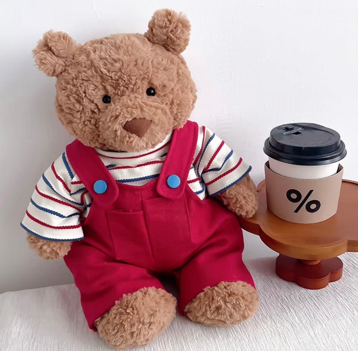 Bartholomew Bear wearing red striped dungaree set, seated next to a coffee cup