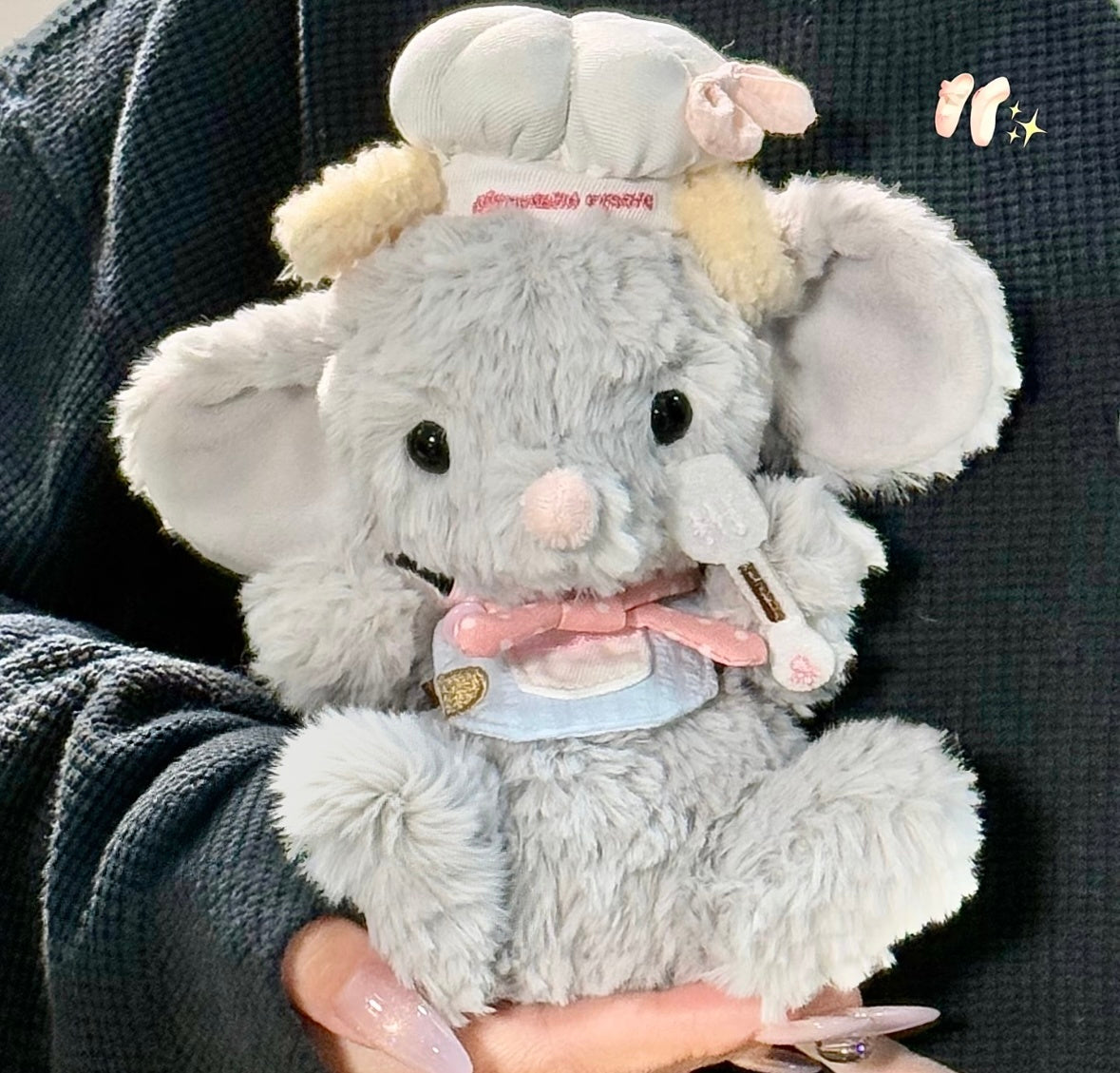 Grey elephant plush wearing a chef hat, pink bow tie and light blue bib outfit