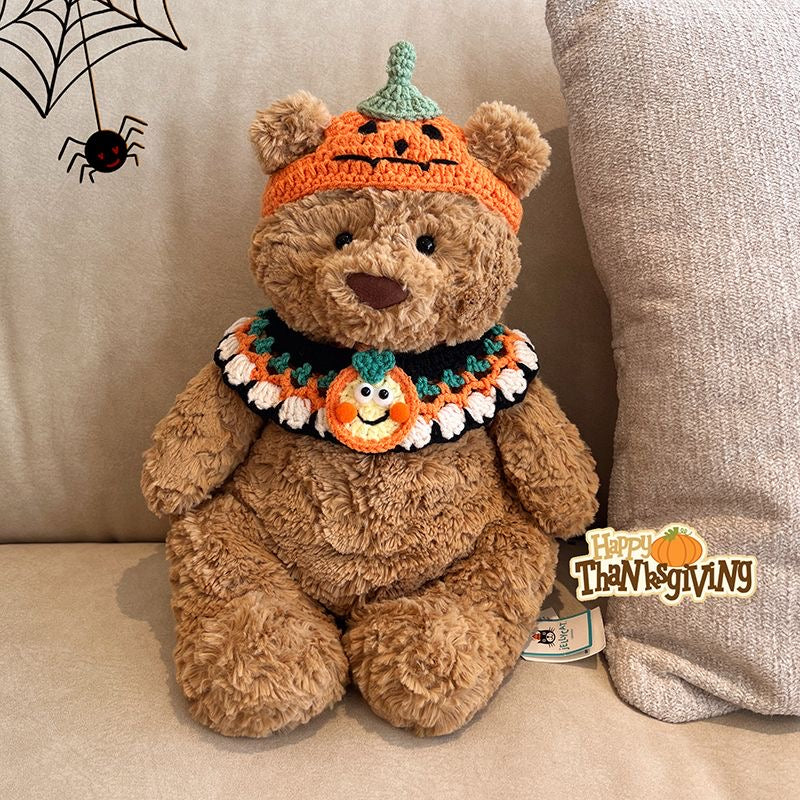 Plush bear wearing a crochet orange pumpkin hat with green stem and a matching pumpkin collar with smiling face