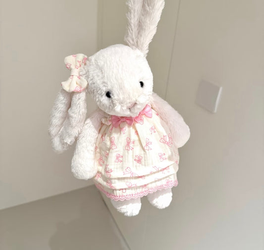 White bunny in pink bow skirt set held in hand, close-up front view