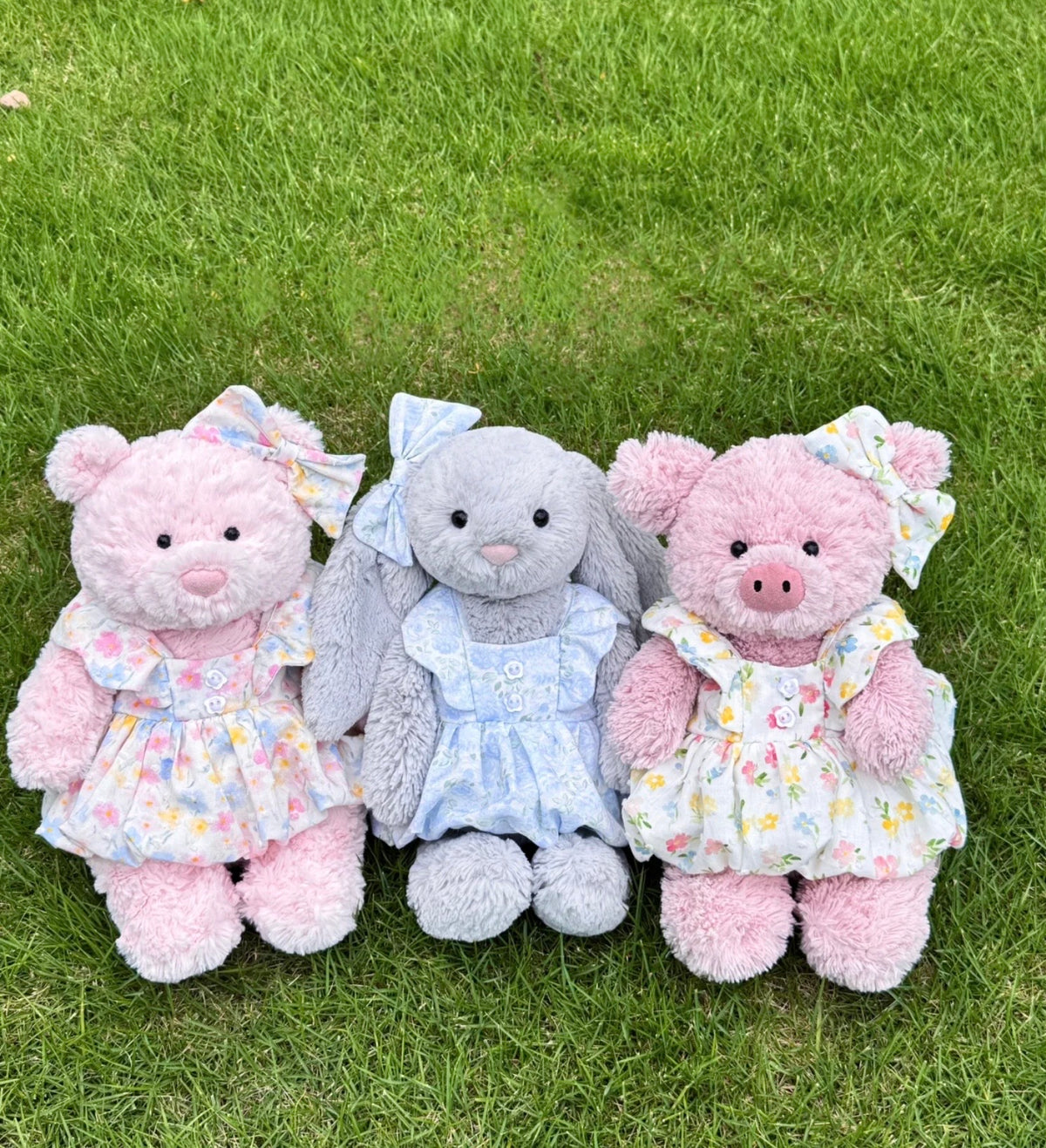 Grey plush bunny outdoors wearing a pale blue floral dress and matching ear bow