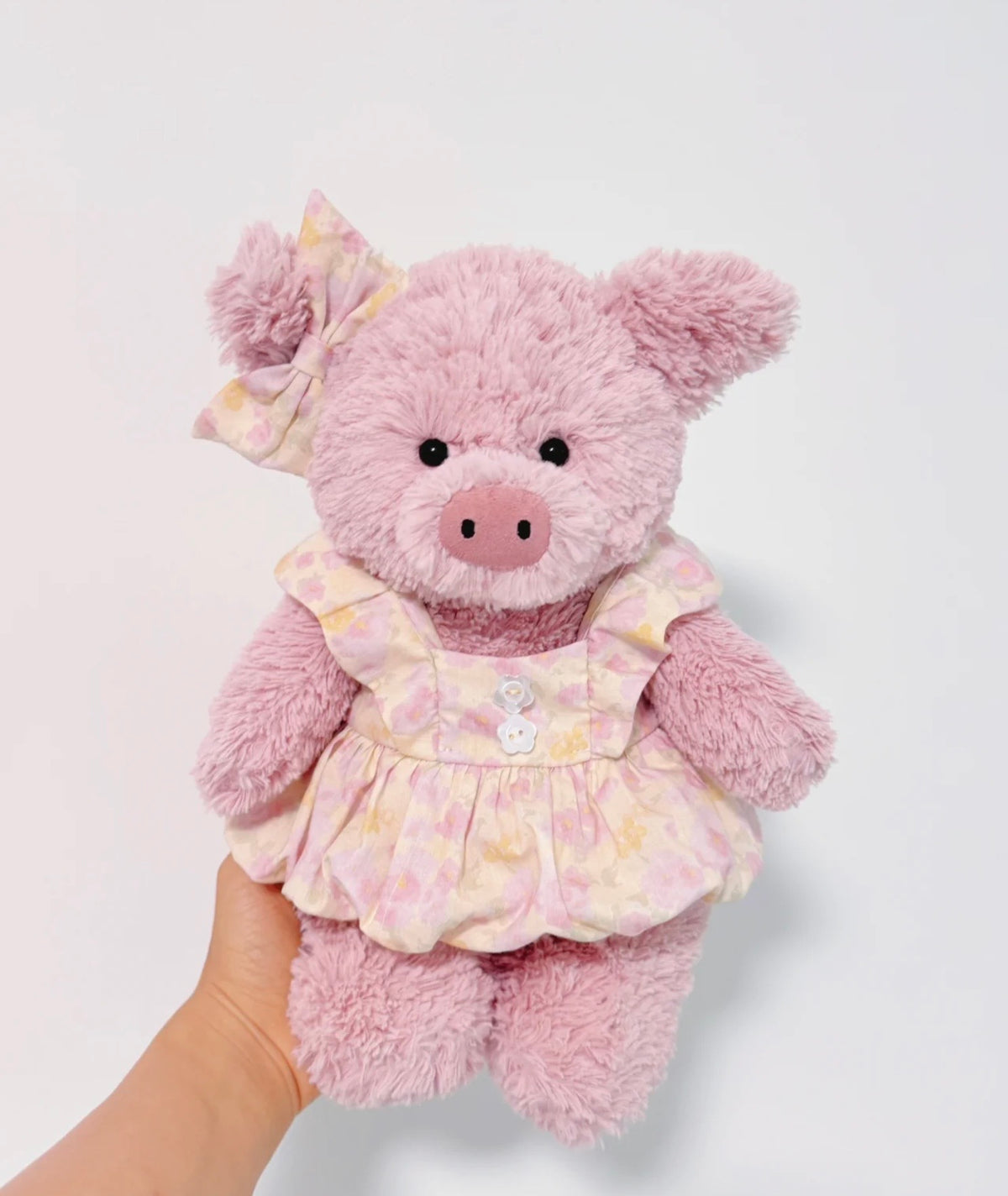Pink plush pig modelling a pale pink and yellow floral dress with flutter shoulders, two front buttons and matching ear bow