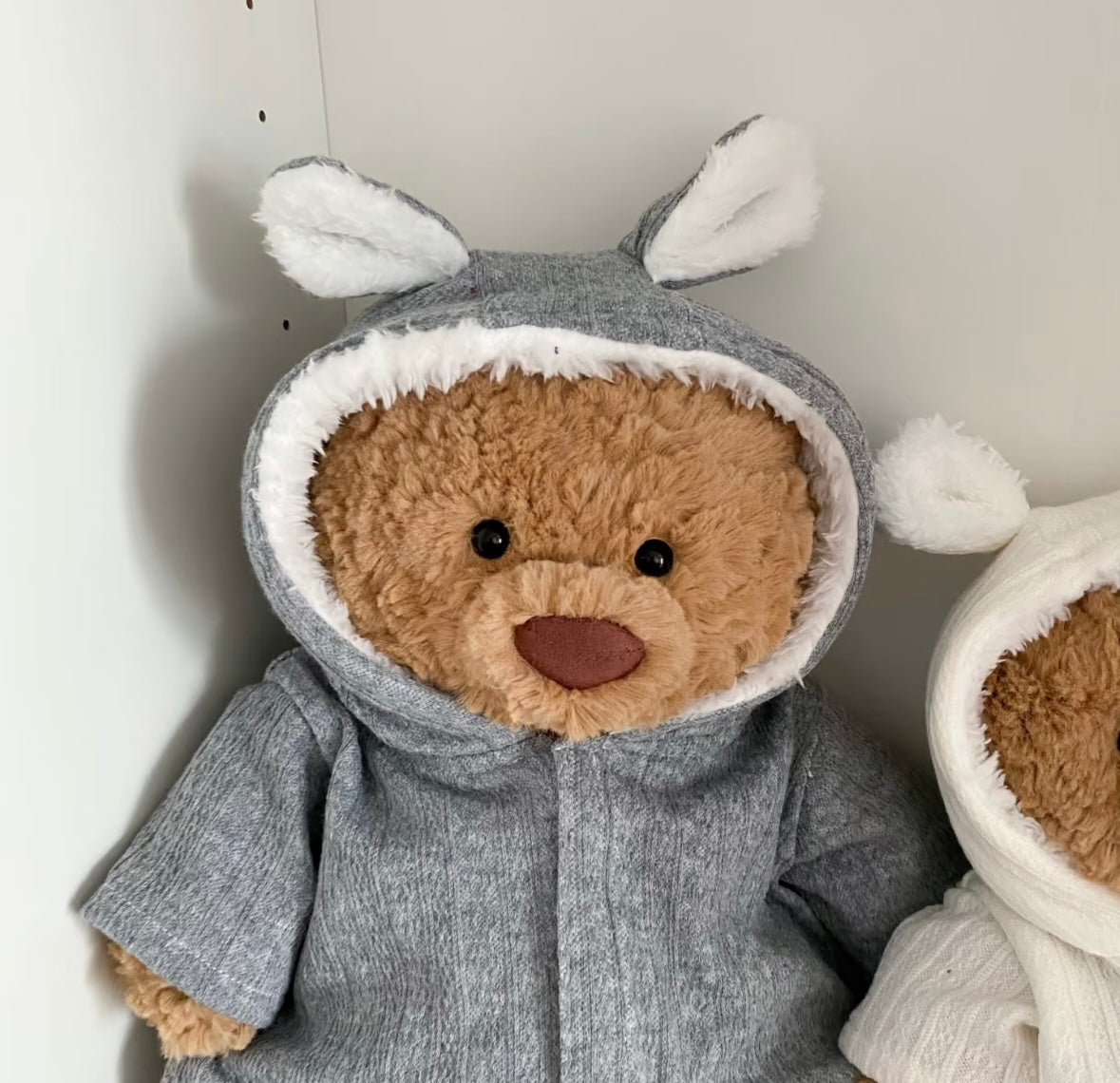 Three teddy bears in grey, cream and blue bunny-ear hooded rompers