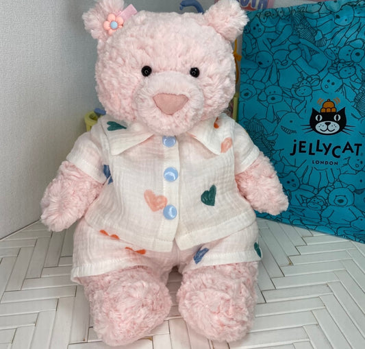 Pink teddy bear wearing cream muslin pyjamas with a multicolour heart print and blue buttons