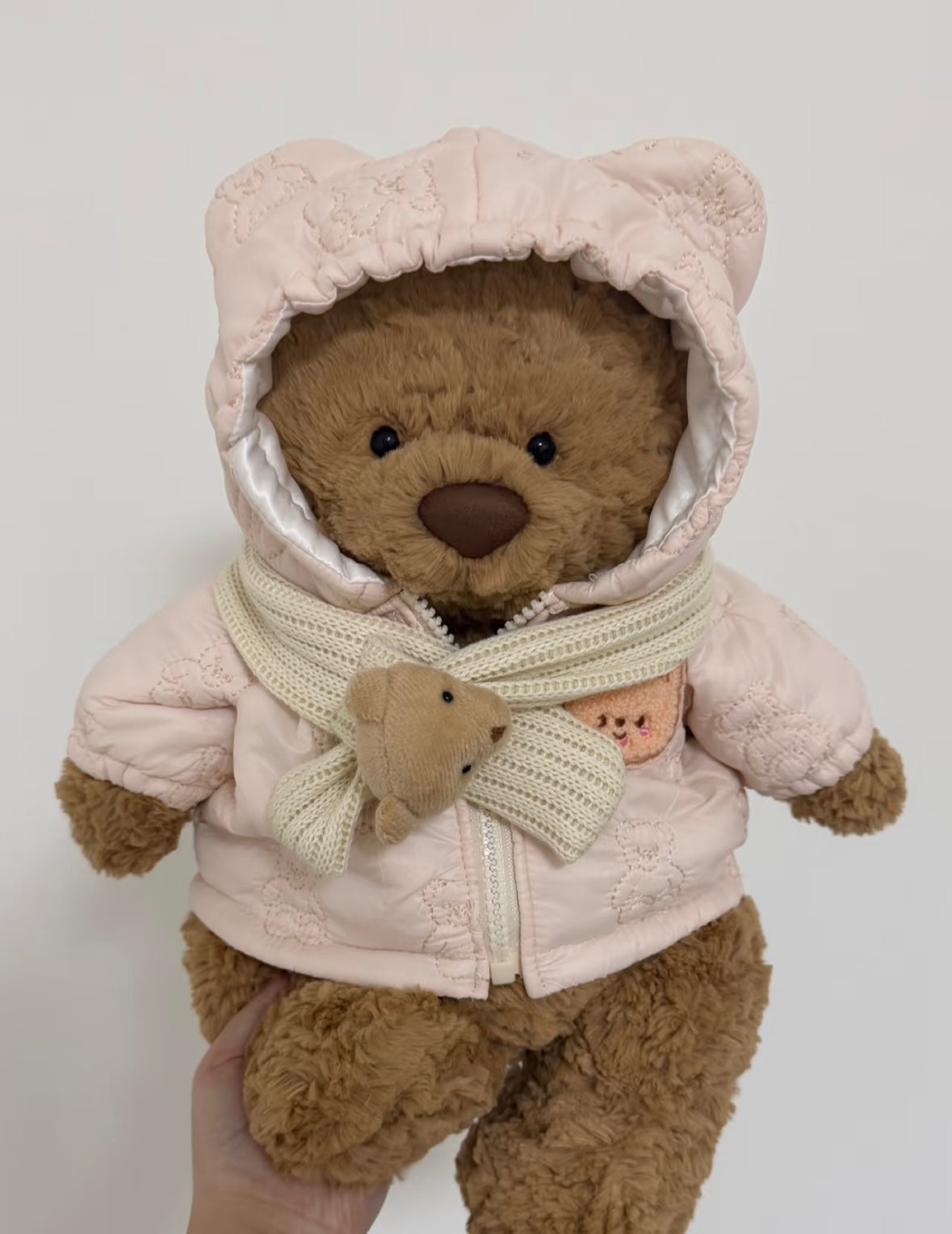 Brown teddy bear wearing a white quilted bear-ear coat with a matching scarf