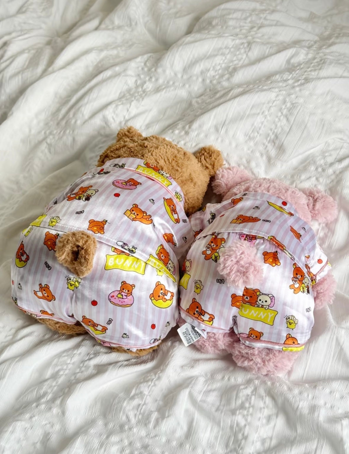 Back view of pink Rilakkuma-print pyjama sets on bear and pig plush toys.
