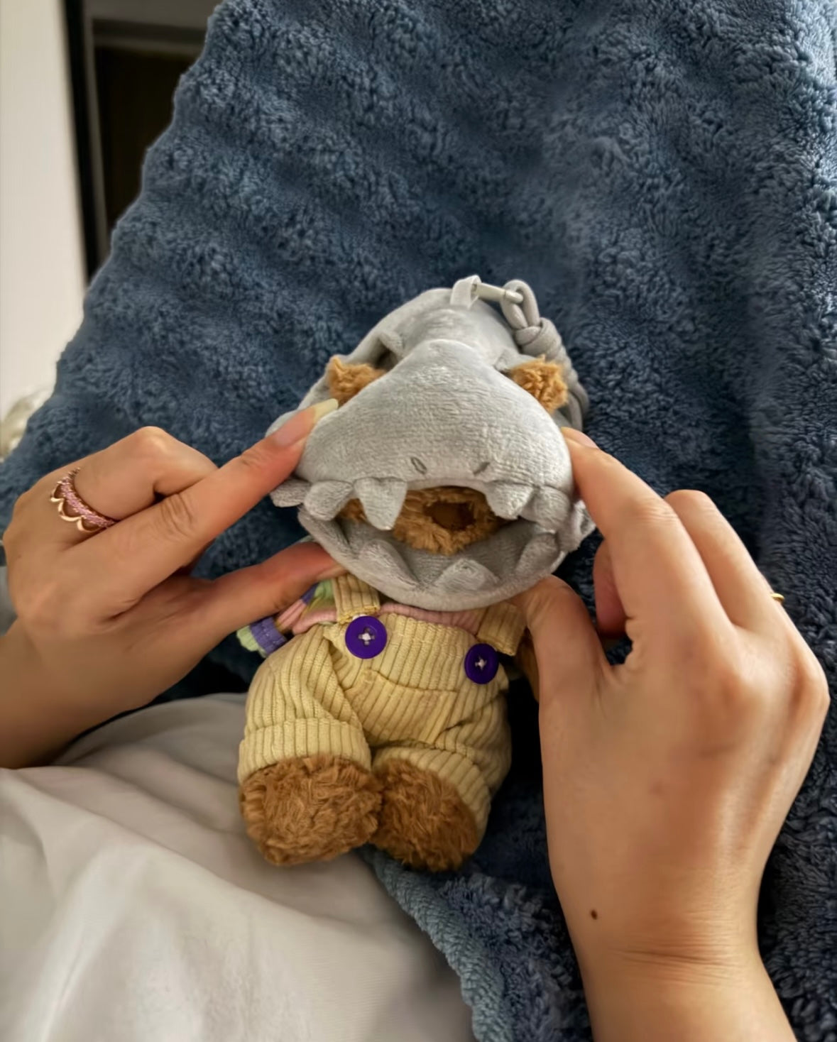 Front view of the shark headpiece with pointed teeth and yellow dungarees with purple buttons on a plush bear
