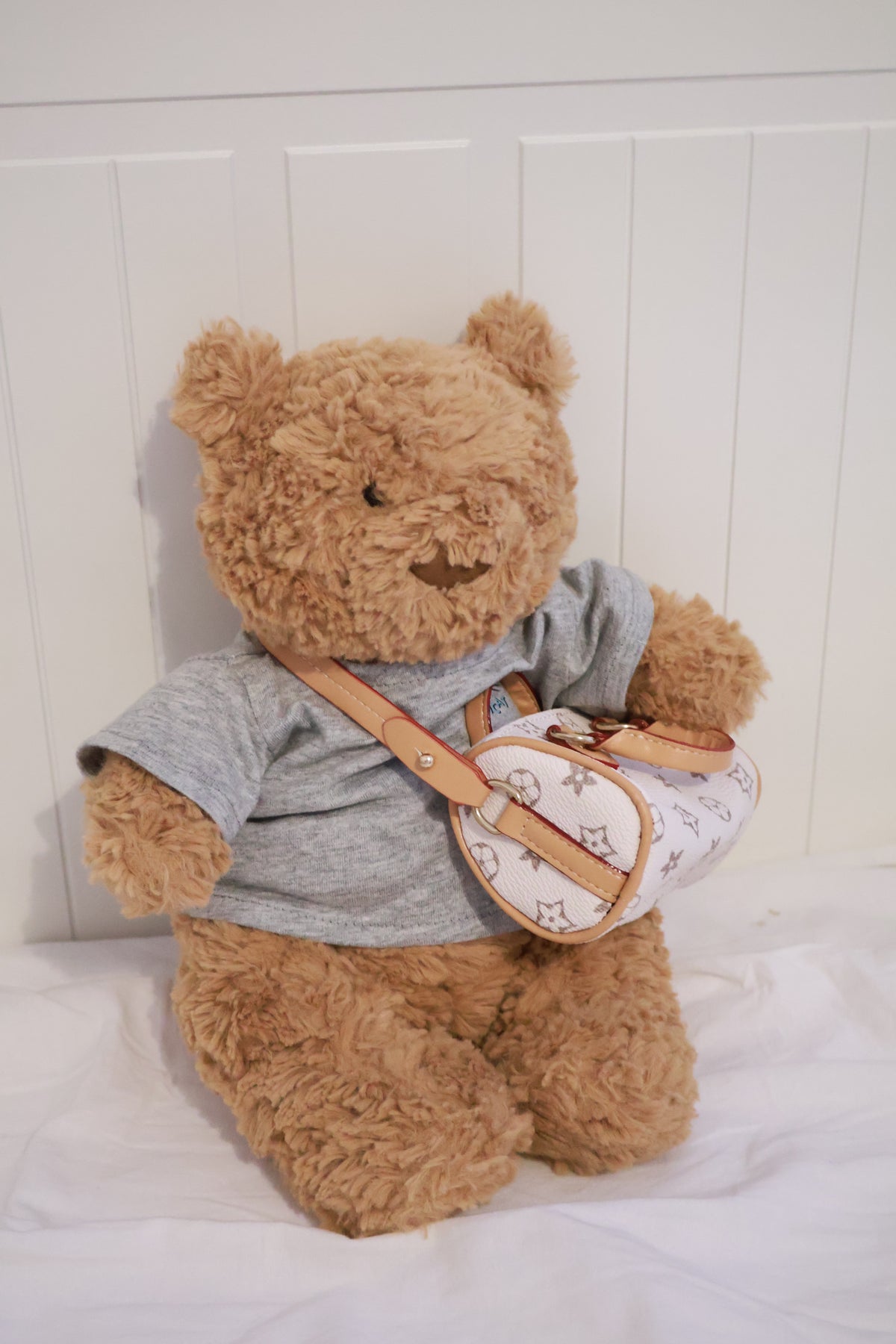 Plush bear in a grey top modelling a white patterned mini handbag