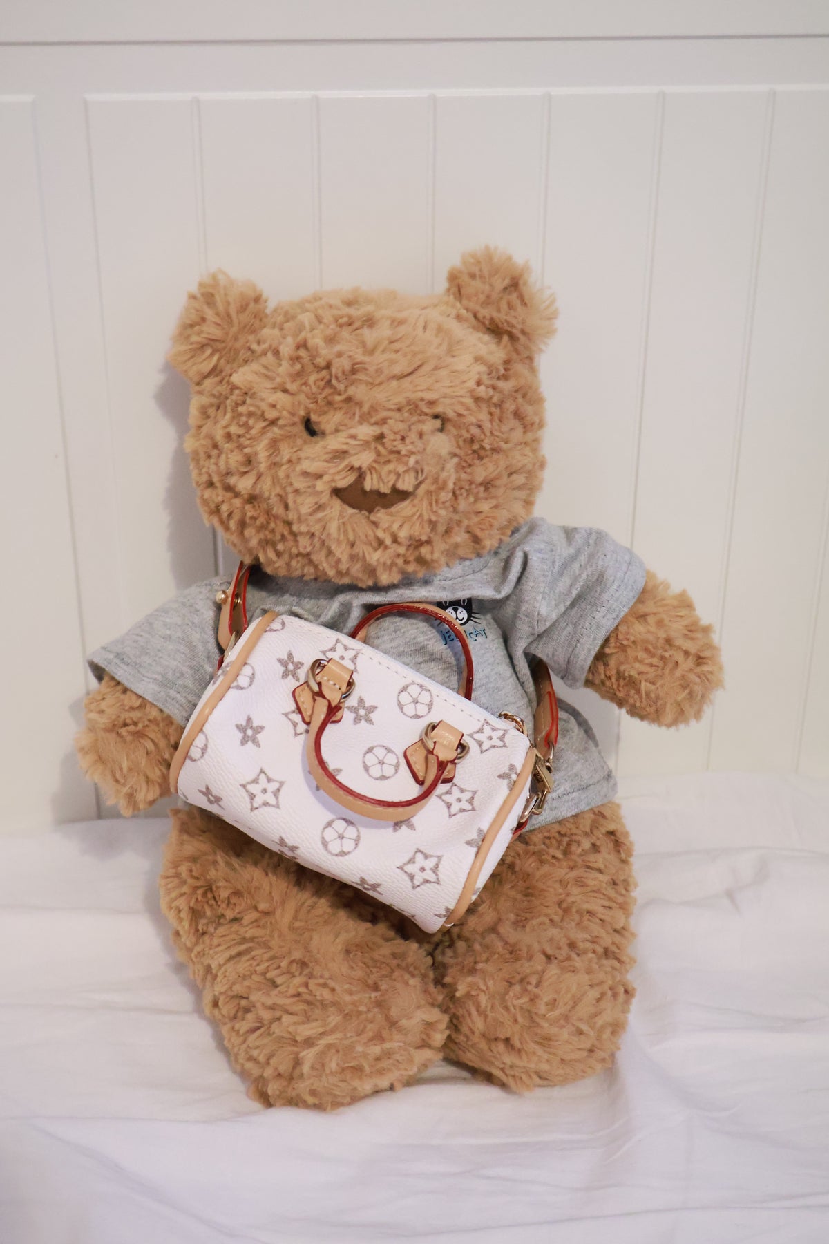 Plush bear wearing the white patterned mini handbag across its body