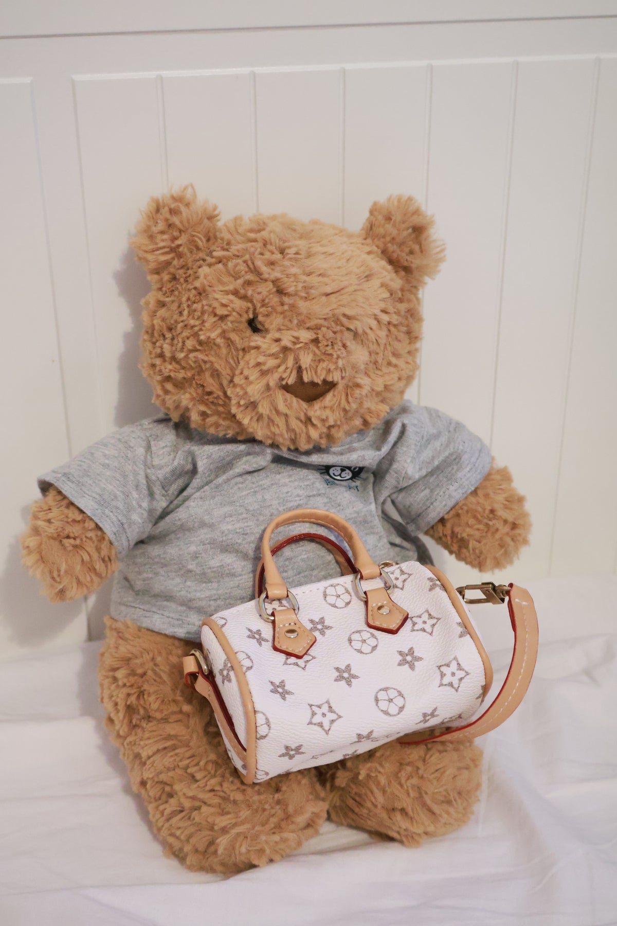 Front view of a plush bear modelling the white patterned mini handbag