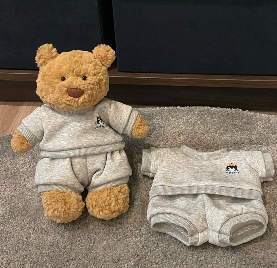 Medium bear wearing grey Jellycat sweatsuit with spare set beside it