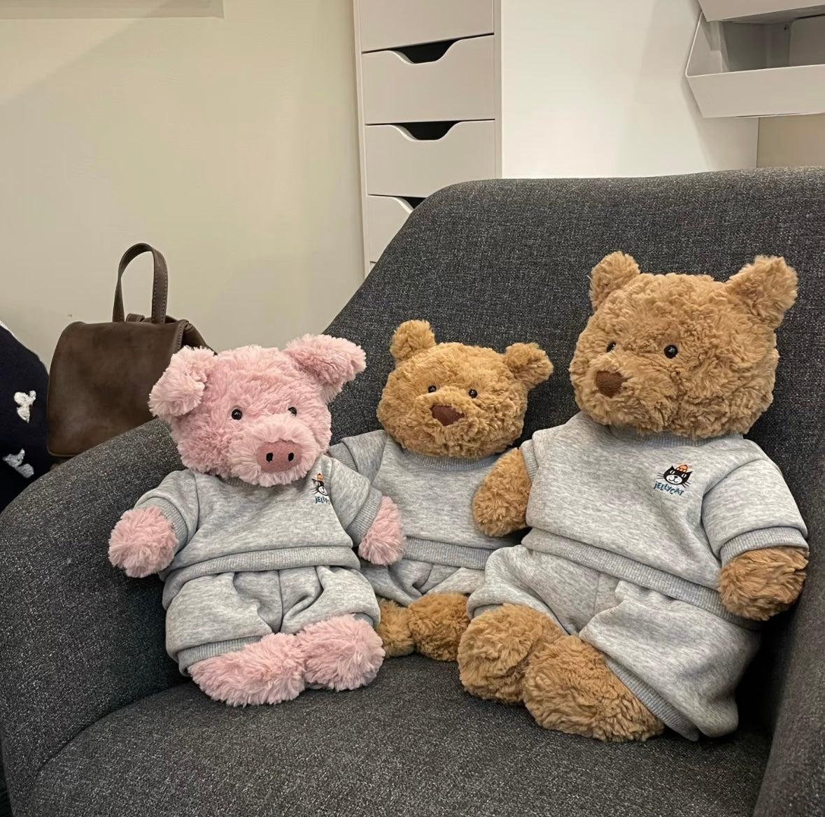 Pink pig, medium bear and large bear all wearing grey Jellycat sweatsuit sets on sofa