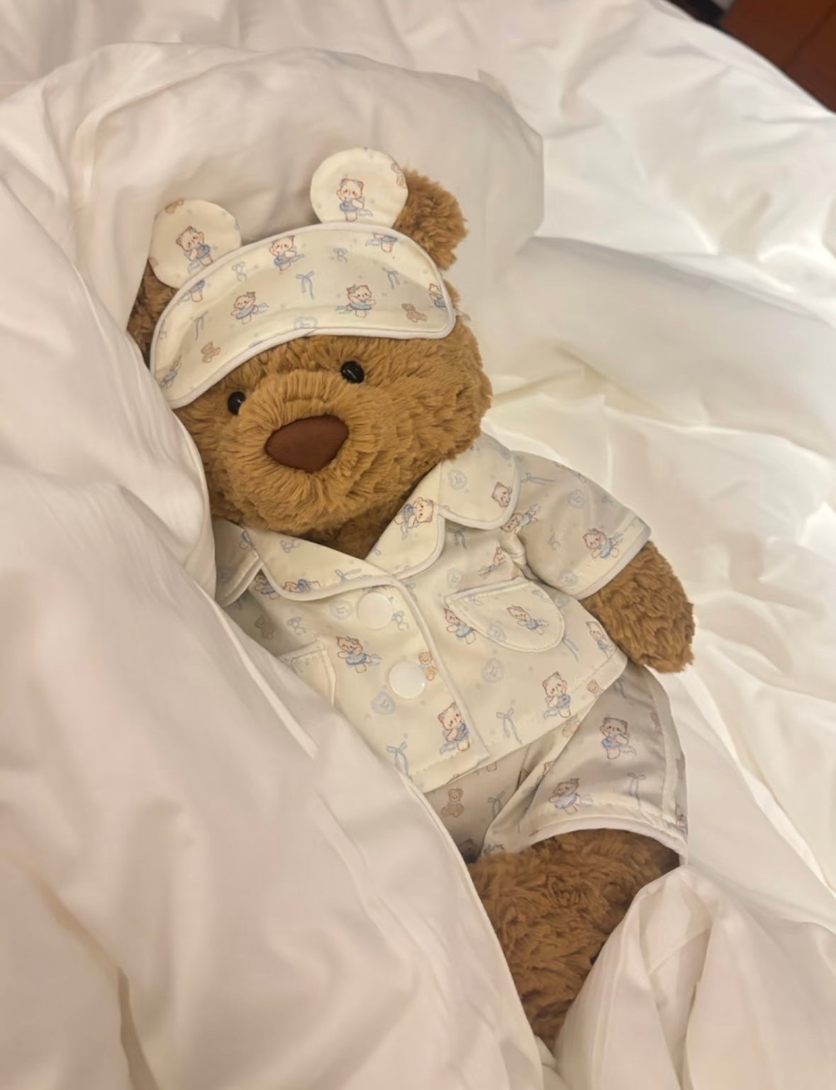 Bartholomew Bear in pyjama set lying on white bedding with sleep mask