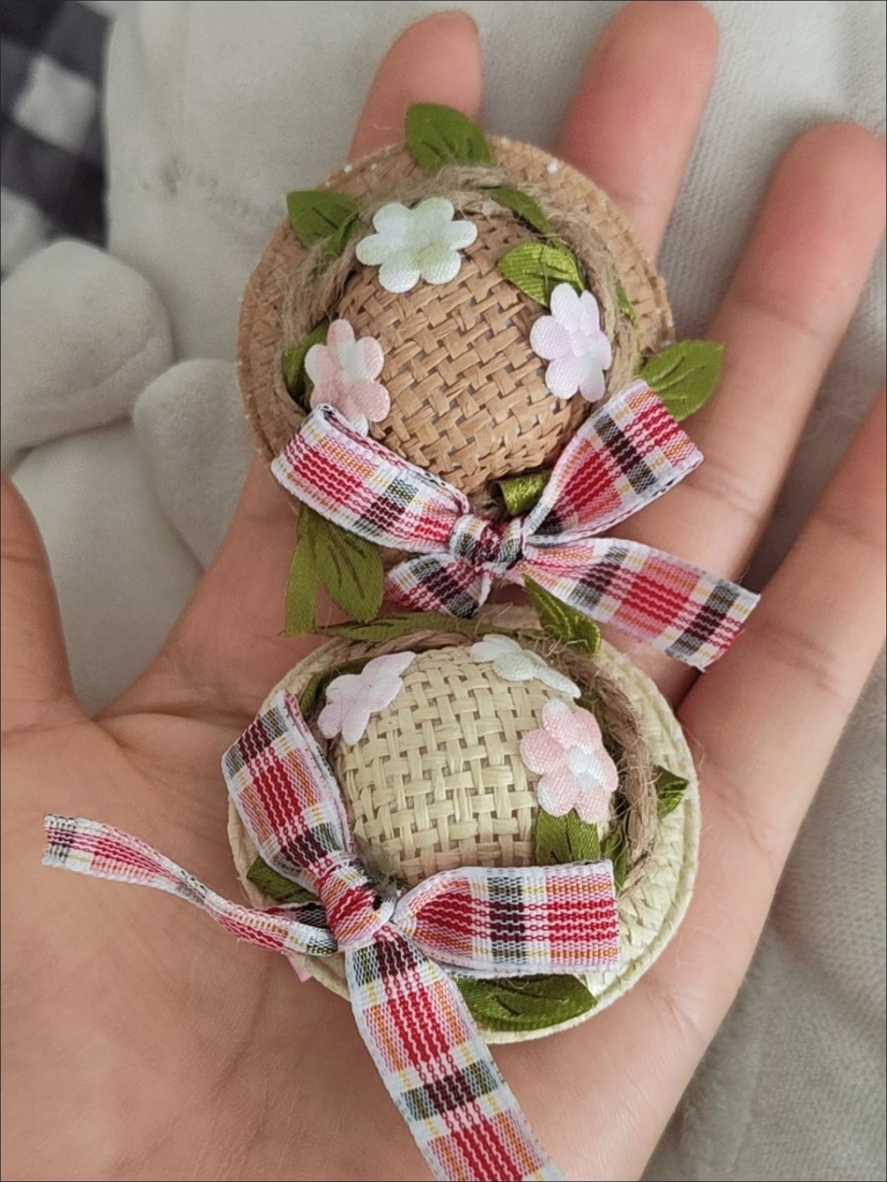 Two mini straw hats with tartan bows held in hand