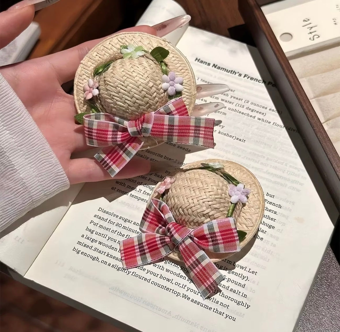 Two mini straw hats with tartan bows displayed on book