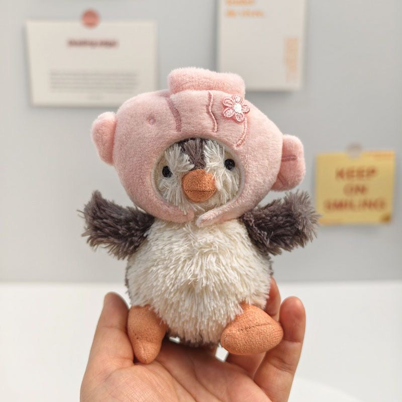 Jellycat Peanut Penguin wearing soft pink pig hoodie hat with embroidered flower