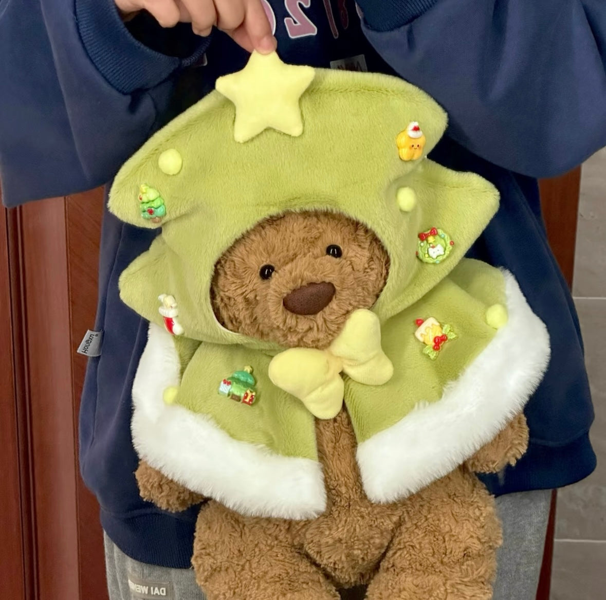 Bartholomew Bear wearing green Christmas tree cape held up showing full outfit