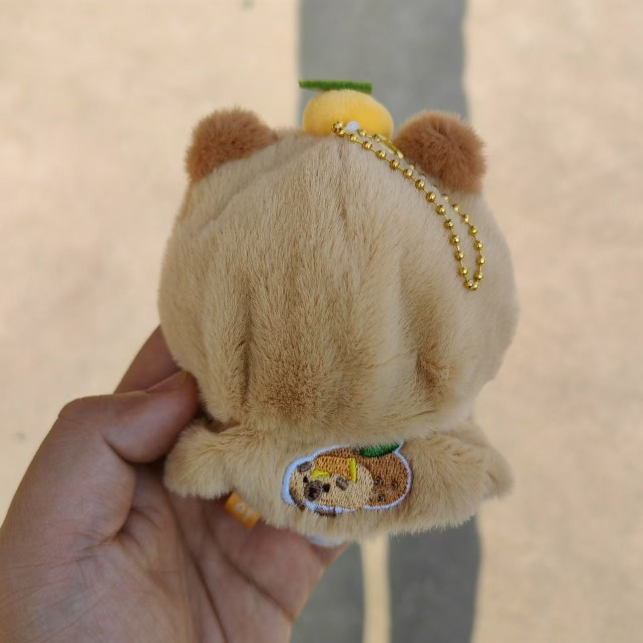 Capybara yuzu plush keychain back view showing embroidered badge and gold chain
