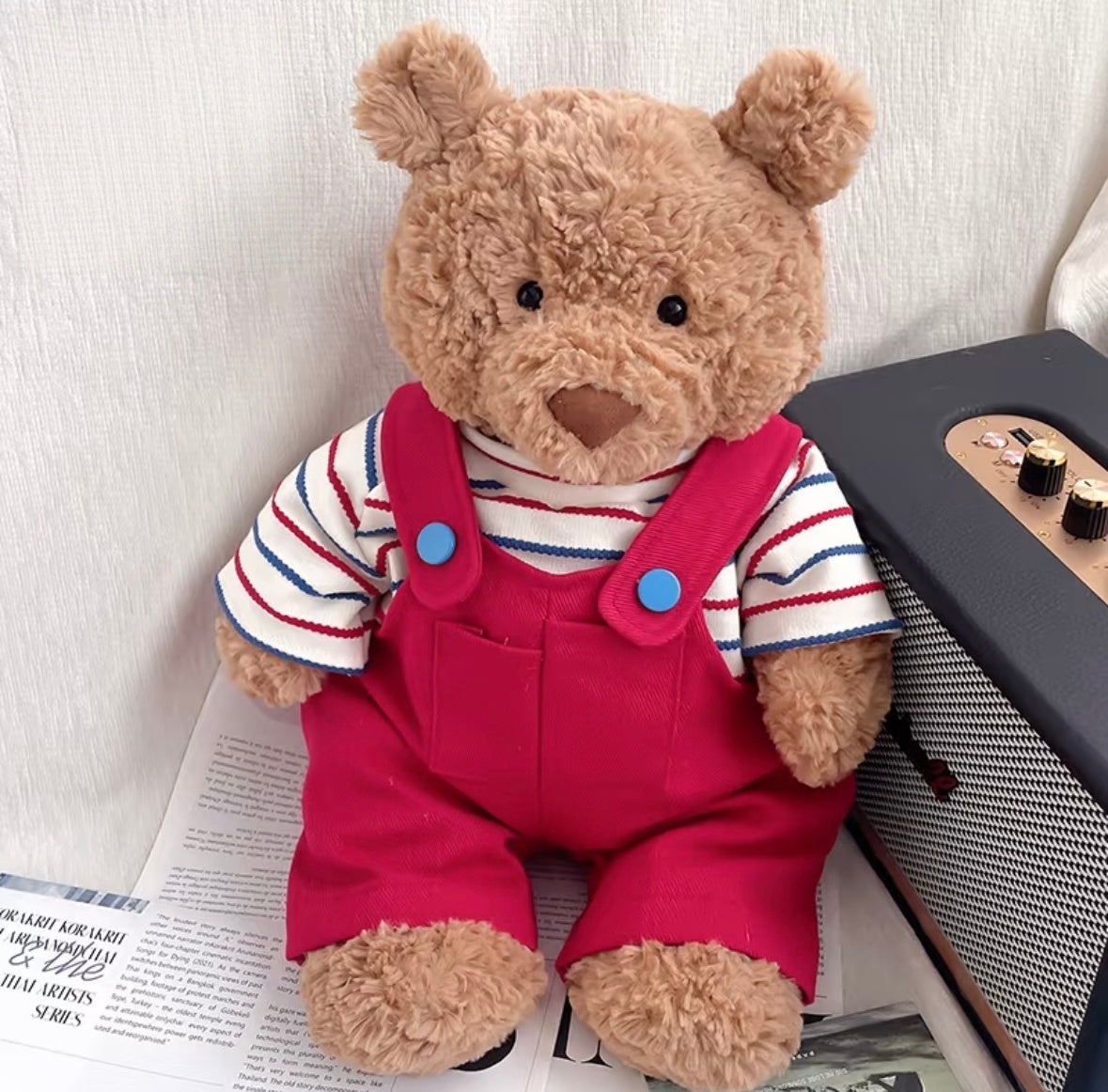 Bartholomew Bear wearing red striped dungaree set, seated next to a vintage radio