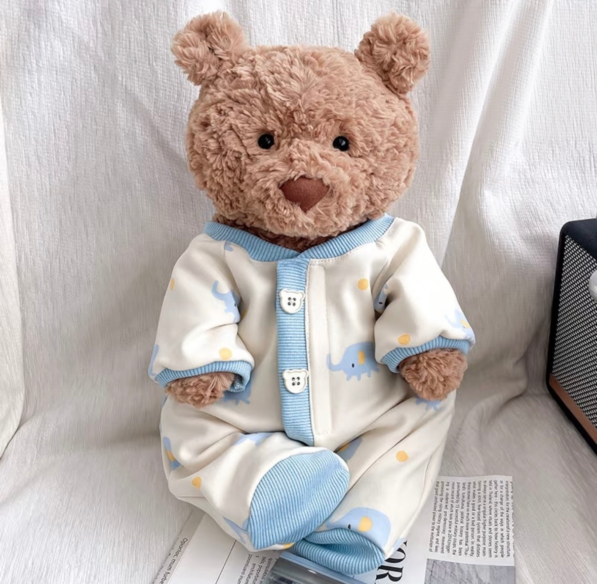 Bartholomew Bear wearing a cream elephant-print sleepsuit with blue ribbed trim and bear-shaped buttons