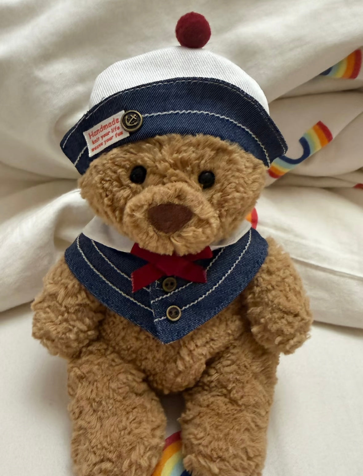 Bartholomew Bear wearing a denim sailor hat and collar set with red bow and gold anchor badge — close-up