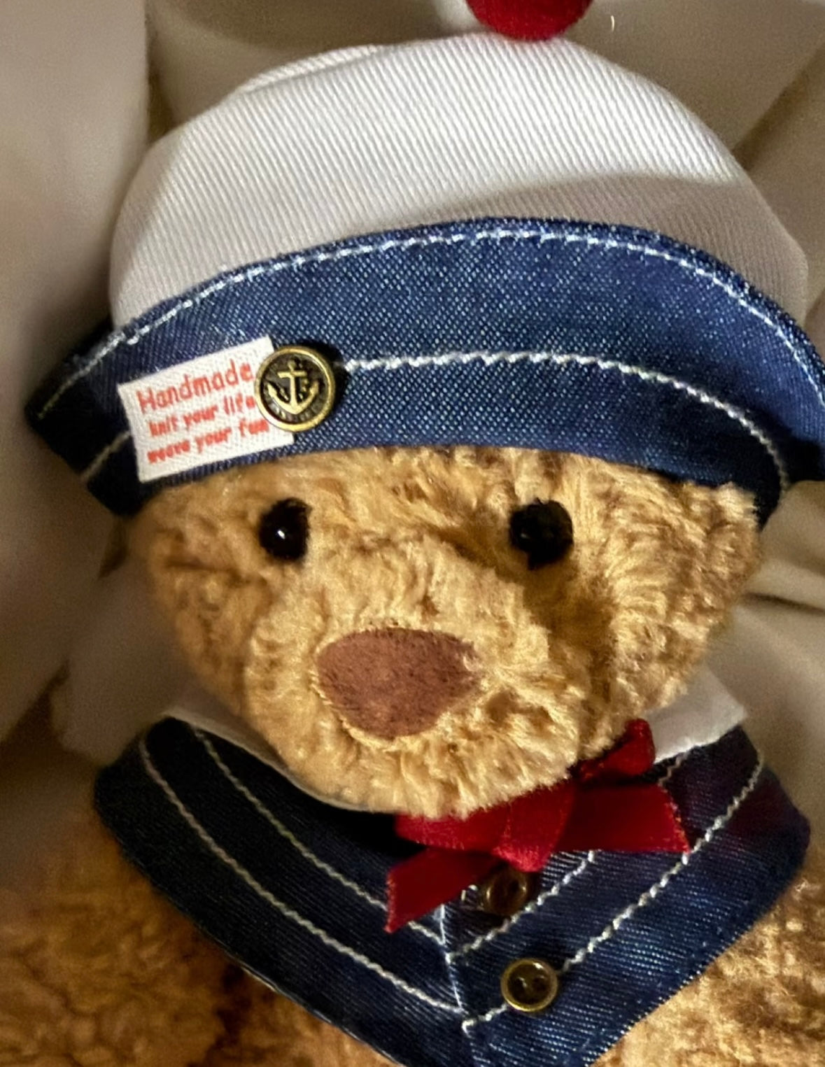 Bartholomew Bear wearing the full denim sailor hat and collar set, seated on white bedding