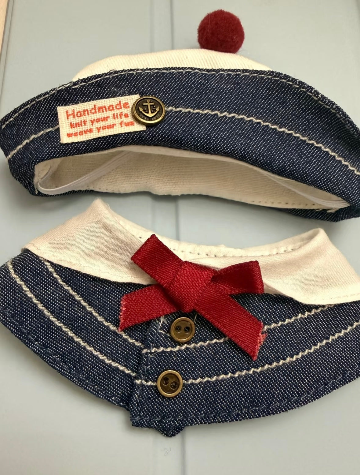 Flat lay of the denim sailor hat and collar set showing the red bow, brass buttons, and anchor badge