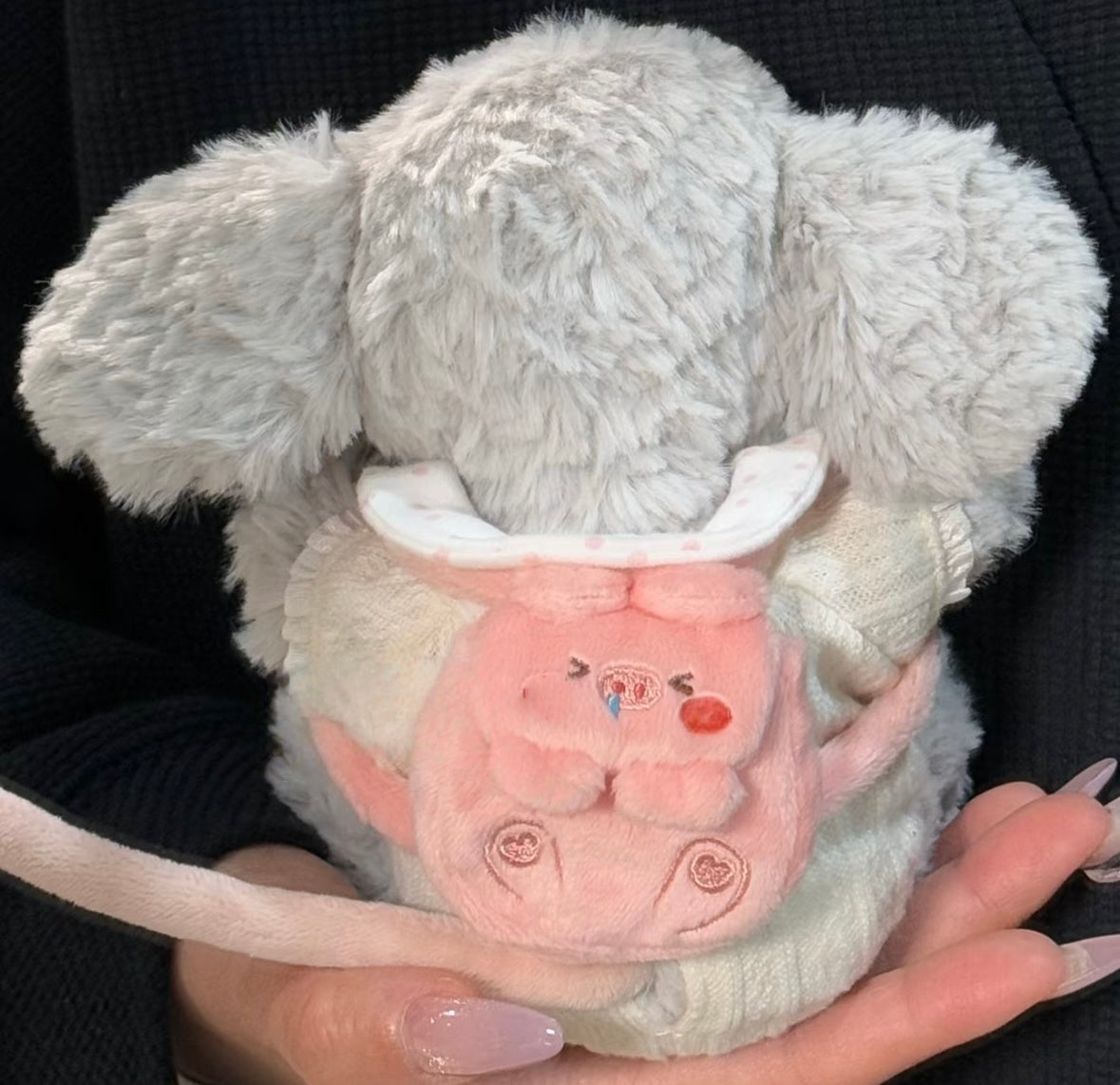 Grey elephant plush wearing a pink piggy backpack with embroidered face and button details