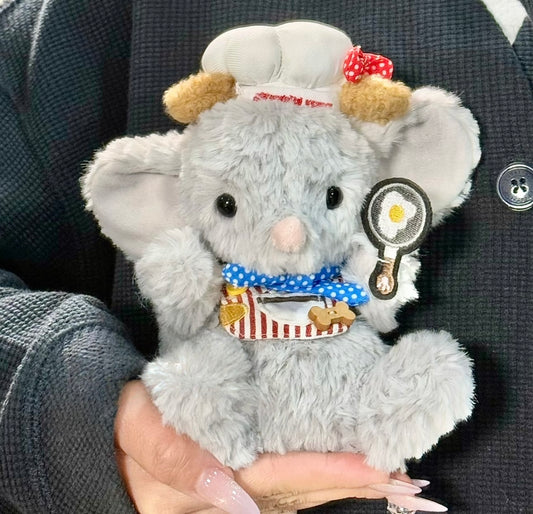 Grey elephant plush wearing a chef hat with red bow, blue polka dot neckerchief, striped apron and holding an embroidered frying pan