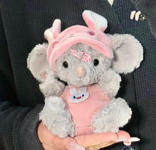 Grey elephant plush wearing a pink bunny hat with ears, pink hair clip and pink bunny-embroidered vest