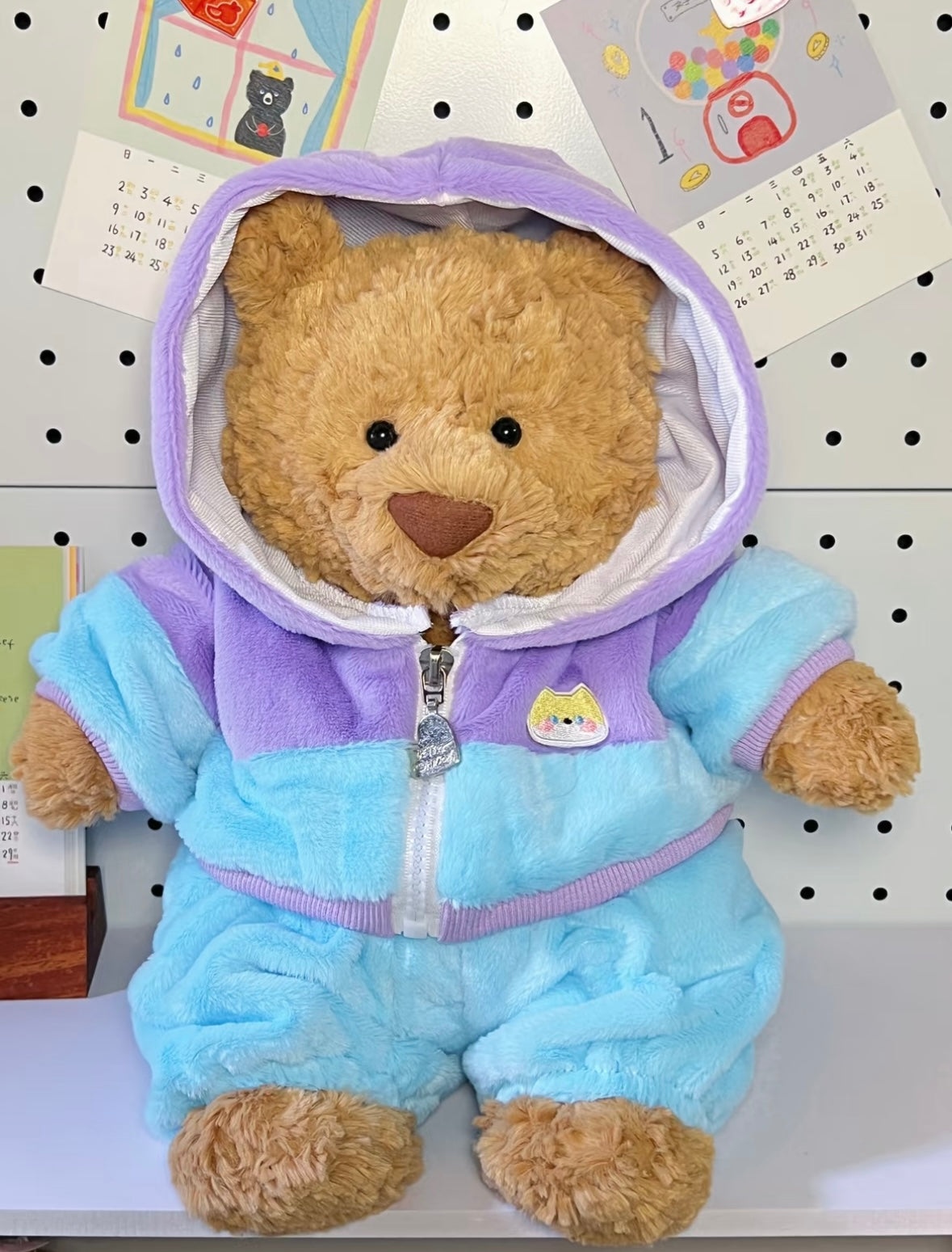 Brown teddy bear wearing pastel blue and lilac hoodie jumpsuit with shiba inu badge - front with hood up