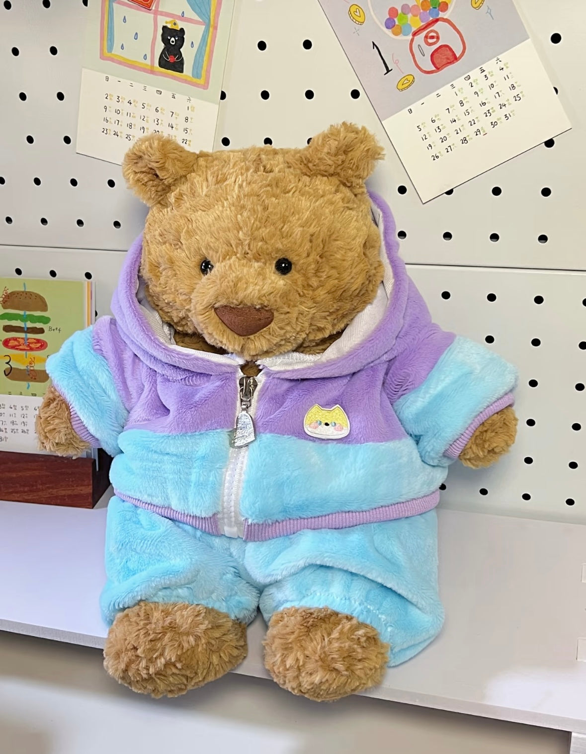 Brown teddy bear wearing pastel blue and lilac hoodie jumpsuit - three quarter view