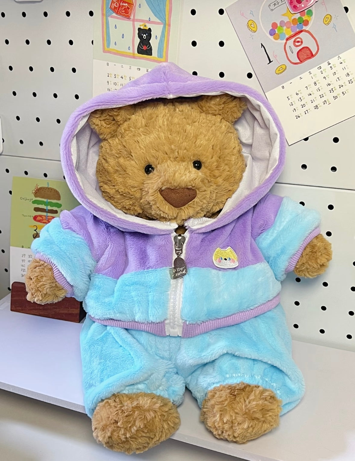 Brown teddy bear wearing pastel blue and lilac hoodie jumpsuit with hood up - full body view