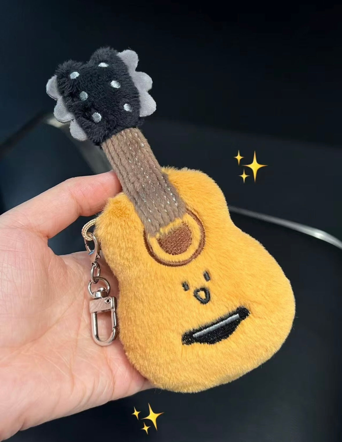 Fluffy golden guitar plush keychain held in hand showing front face and silver clasp