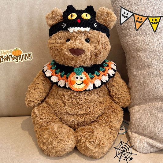 Plush bear wearing a crochet black cat hat with yellow eyes and a pumpkin collar with smiling jack-o-lantern detail