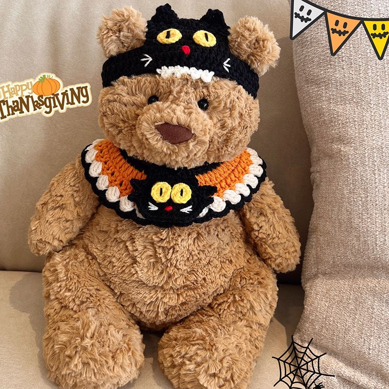 Plush bear wearing a crochet black cat headband with yellow eyes and whiskers, and a matching black and orange cat face collar