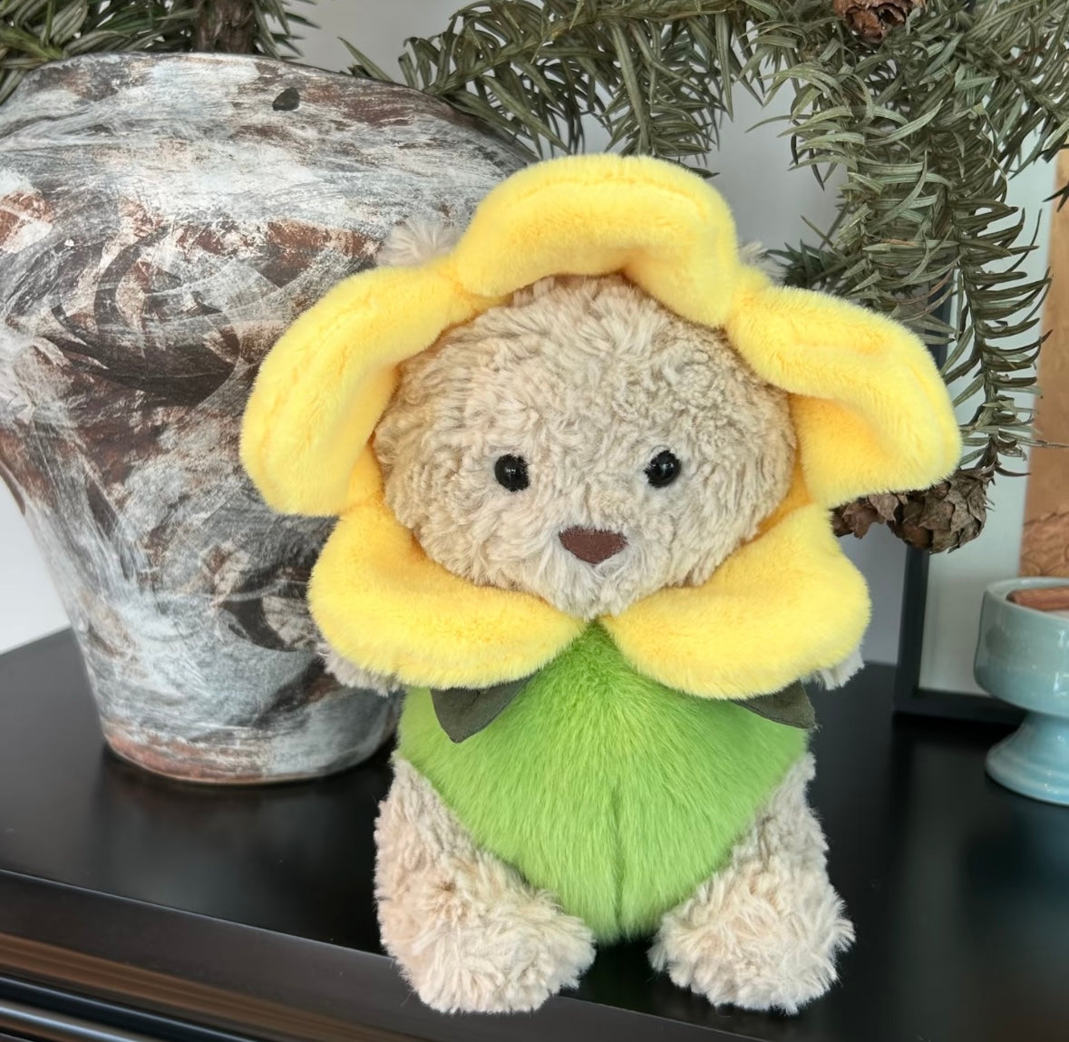 Plush bear in sunflower costume sitting among daisies and hydrangeas in a garden