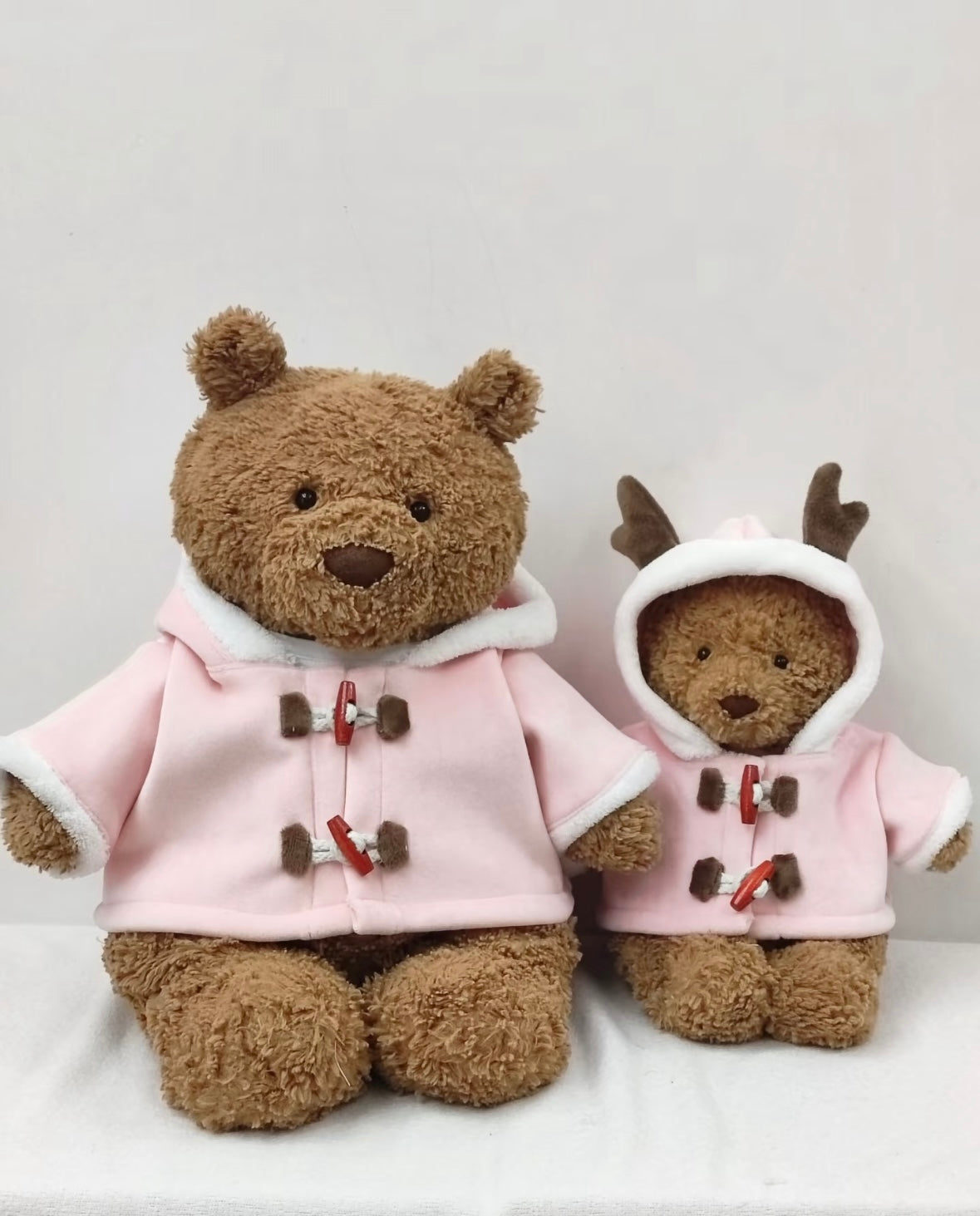 Large Bartholomew Bear and Jellycat Reindeer both wearing pink duffle coats - front size comparison