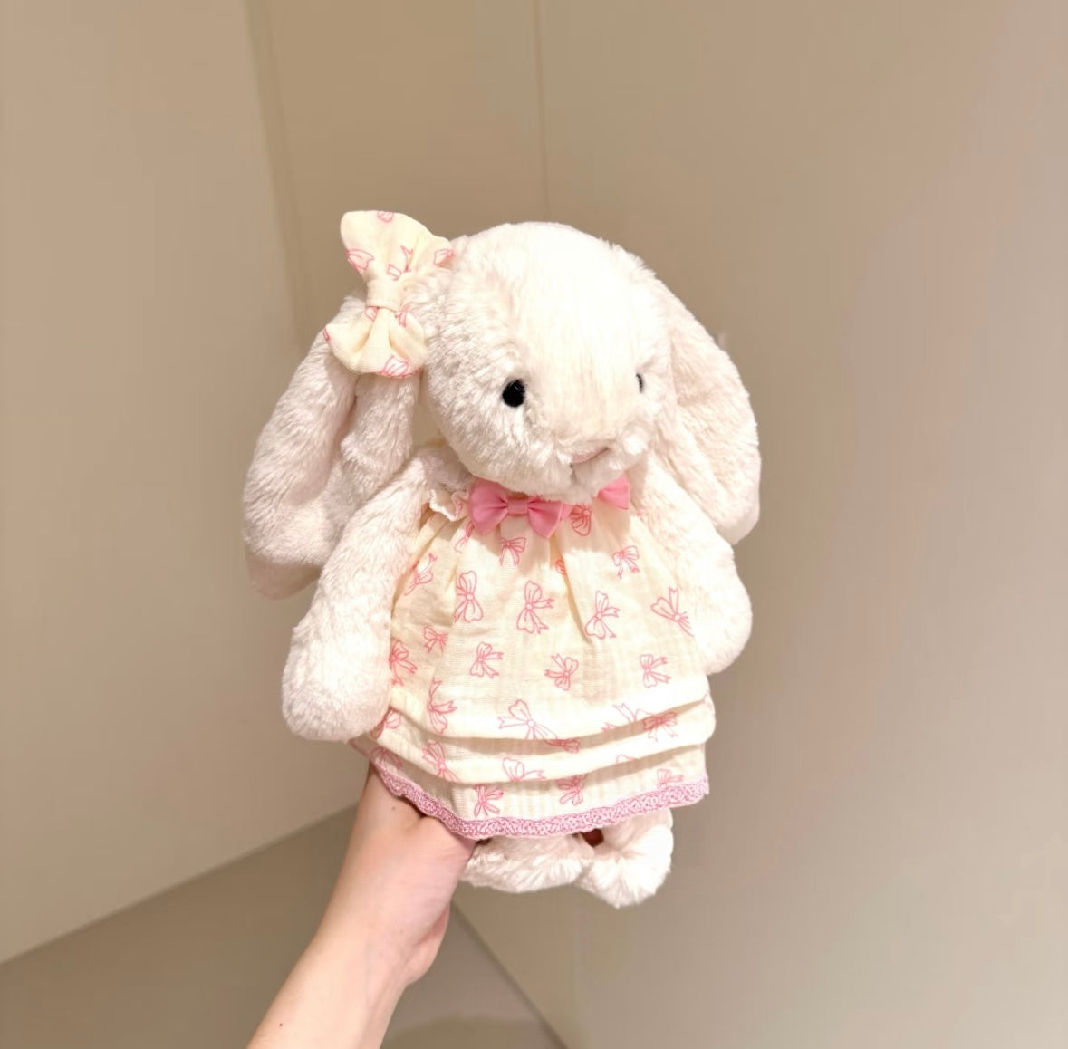 White bunny plush wearing pink bow print skirt set with velvet bow tie, front view