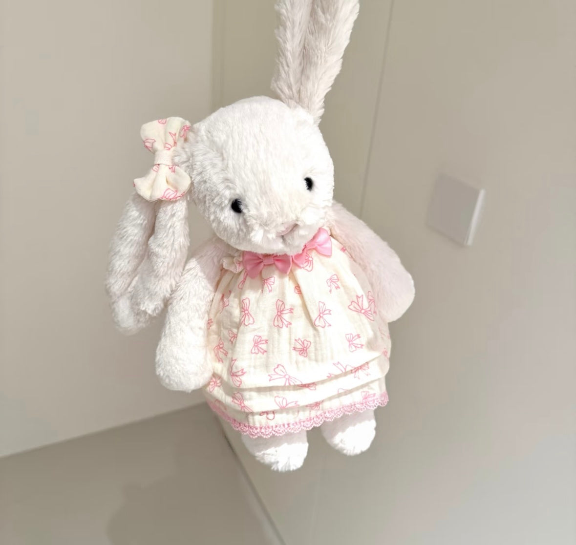 White bunny in pink bow skirt set held in hand, close-up front view