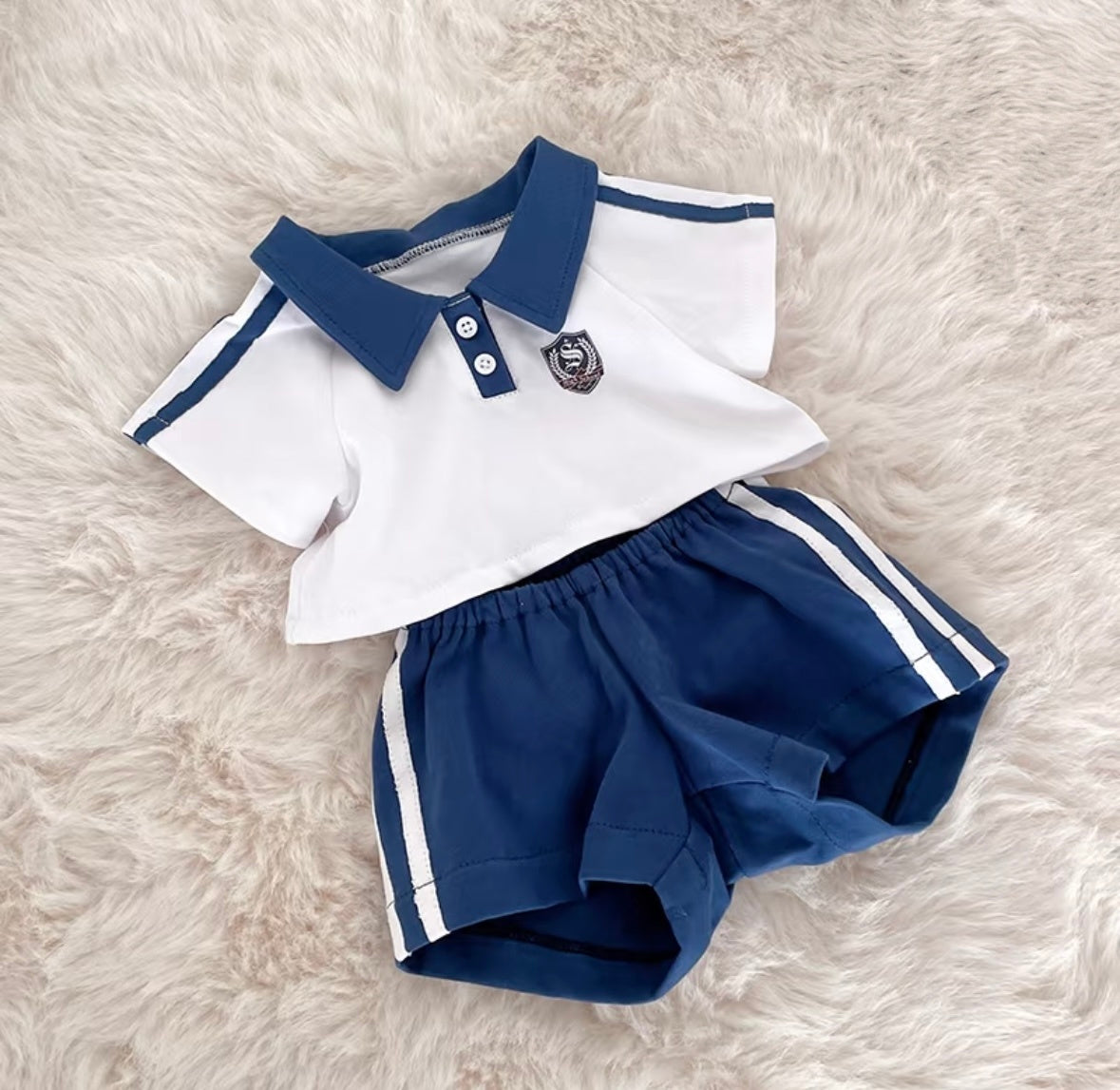 Flat lay of navy polo sport set showing white polo with crest badge and navy shorts with white stripes