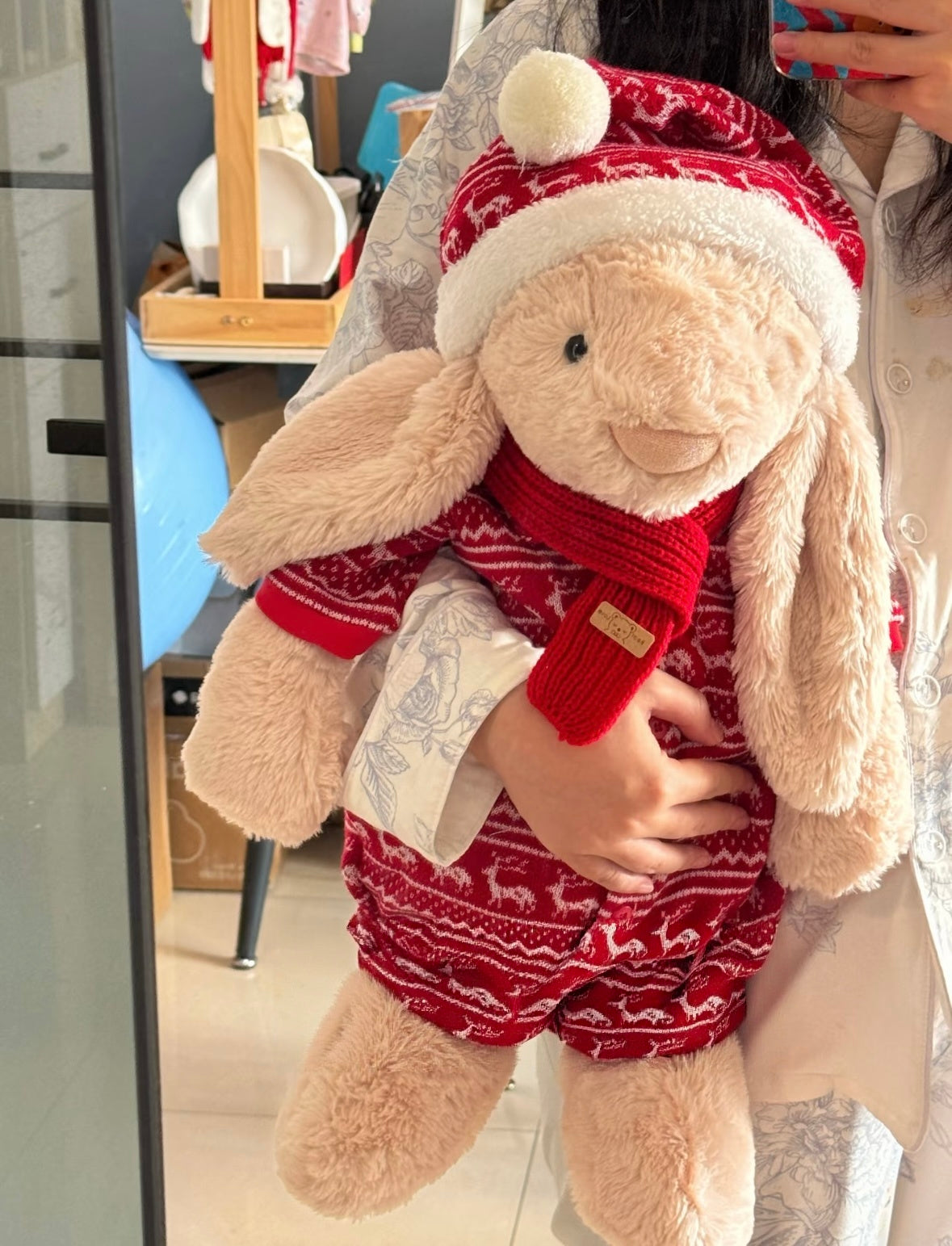 Bashful Bunny wearing red reindeer Fair Isle knit sweater with red scarf and Santa hat, front view held by person