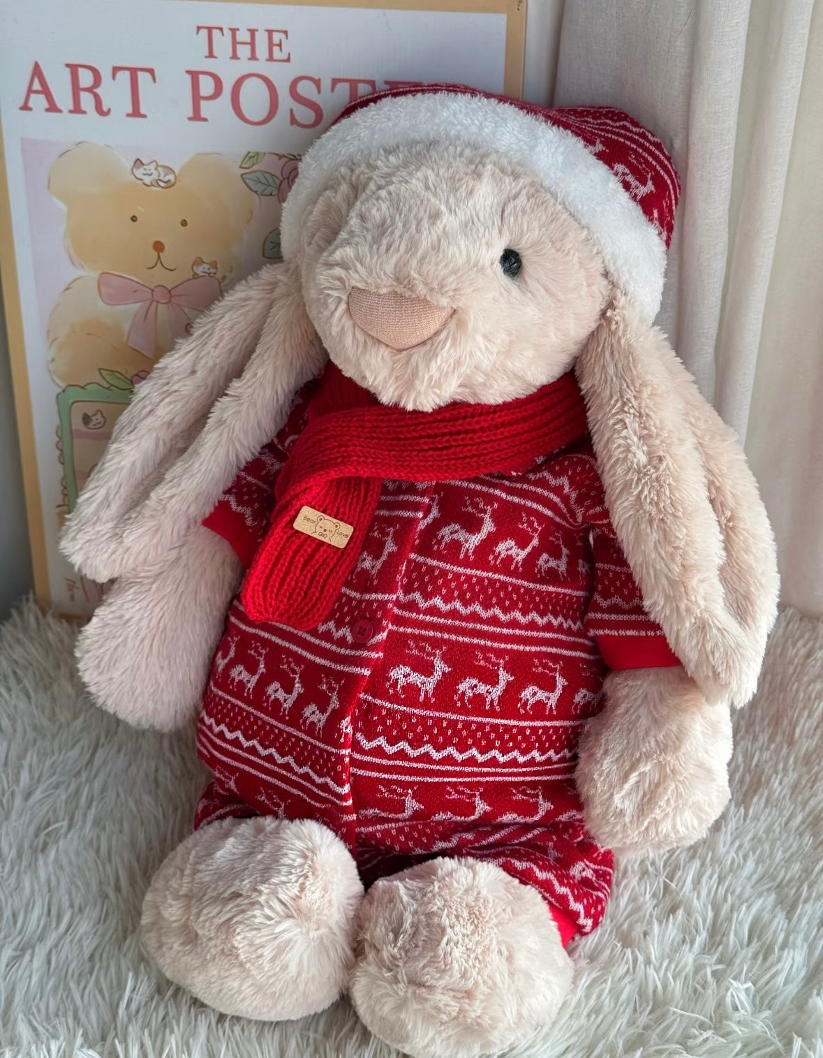 Bashful Bunny in red Christmas reindeer knit set seated against art poster with white fur rug, front view