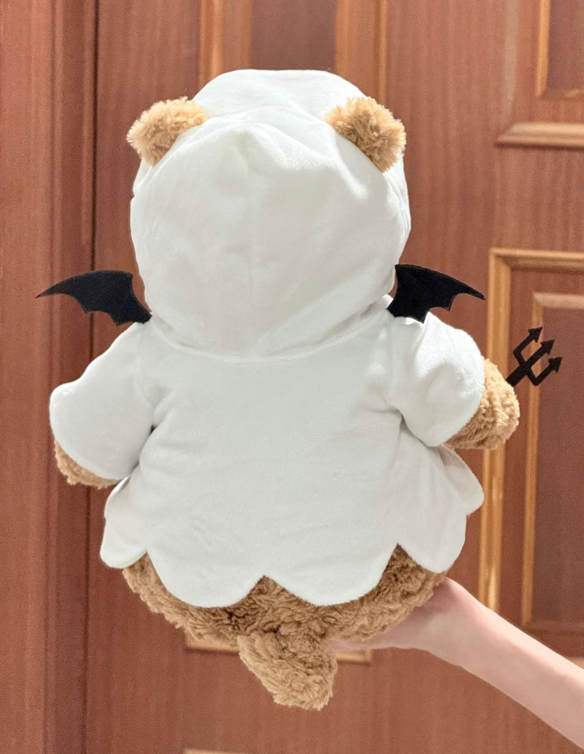 Back view of plush bear in white ghost hoodie showing black bat wings attached to back