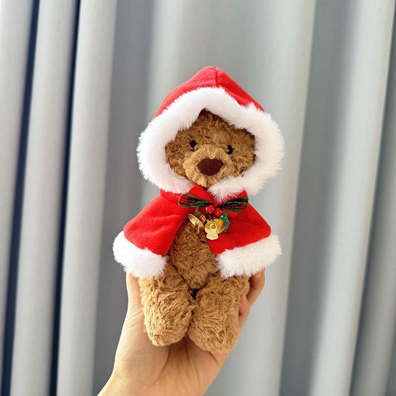 Brown plush bear wearing red velvet hooded Christmas cape with white faux-fur trim and golden jingle bell bow