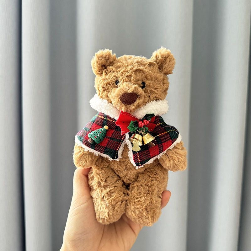 Brown plush bear wearing red and green tartan Christmas cape with white faux-fur trim, red bow, Christmas tree charm and golden jingle bells