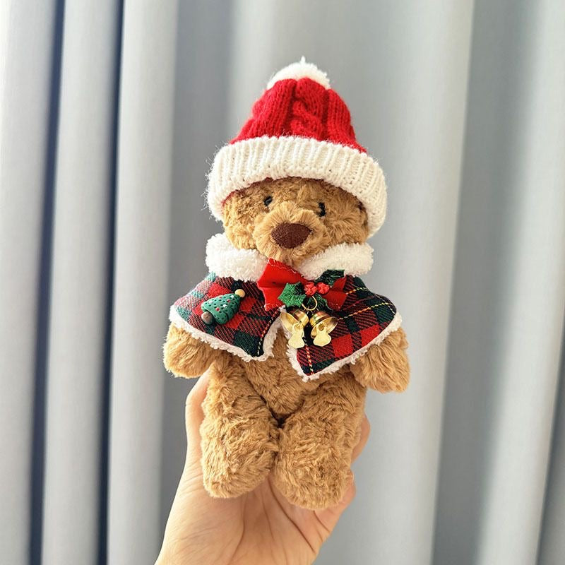 Brown plush bear wearing red and green tartan Christmas cape with white faux-fur trim and knitted red Santa hat with white pom-pom