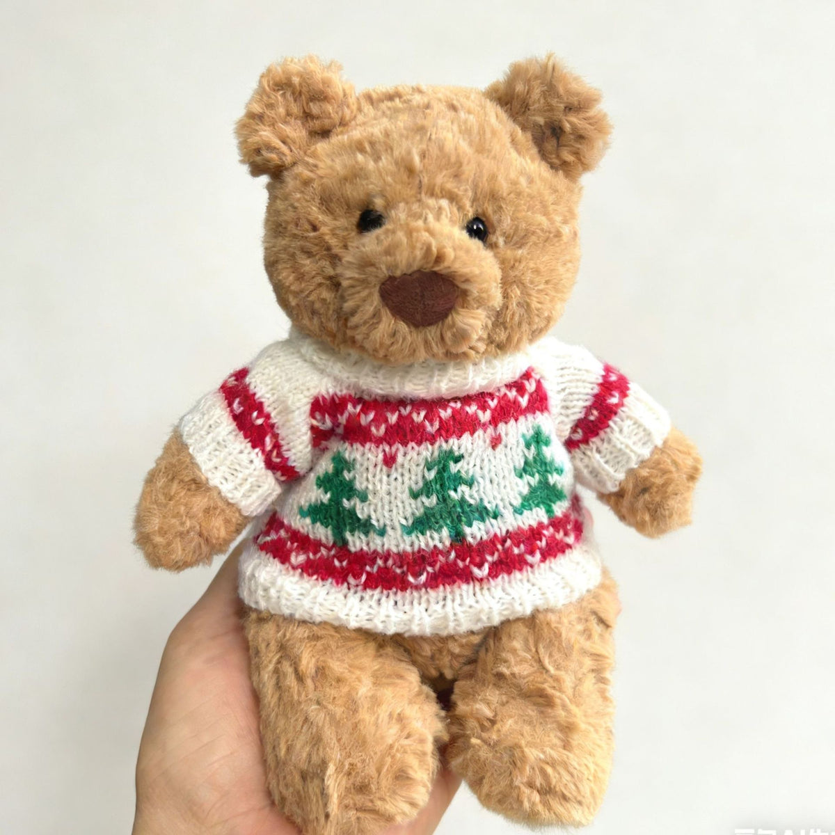 Brown plush bear wearing cream knitted Christmas tree jumper with red and white stripes and green tree motifs