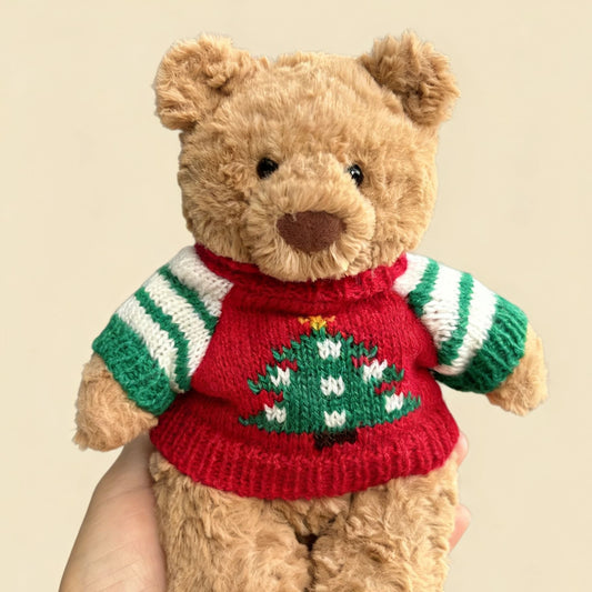 Brown plush bear wearing red knitted Christmas jumper with large embroidered Christmas tree and green and white striped sleeves